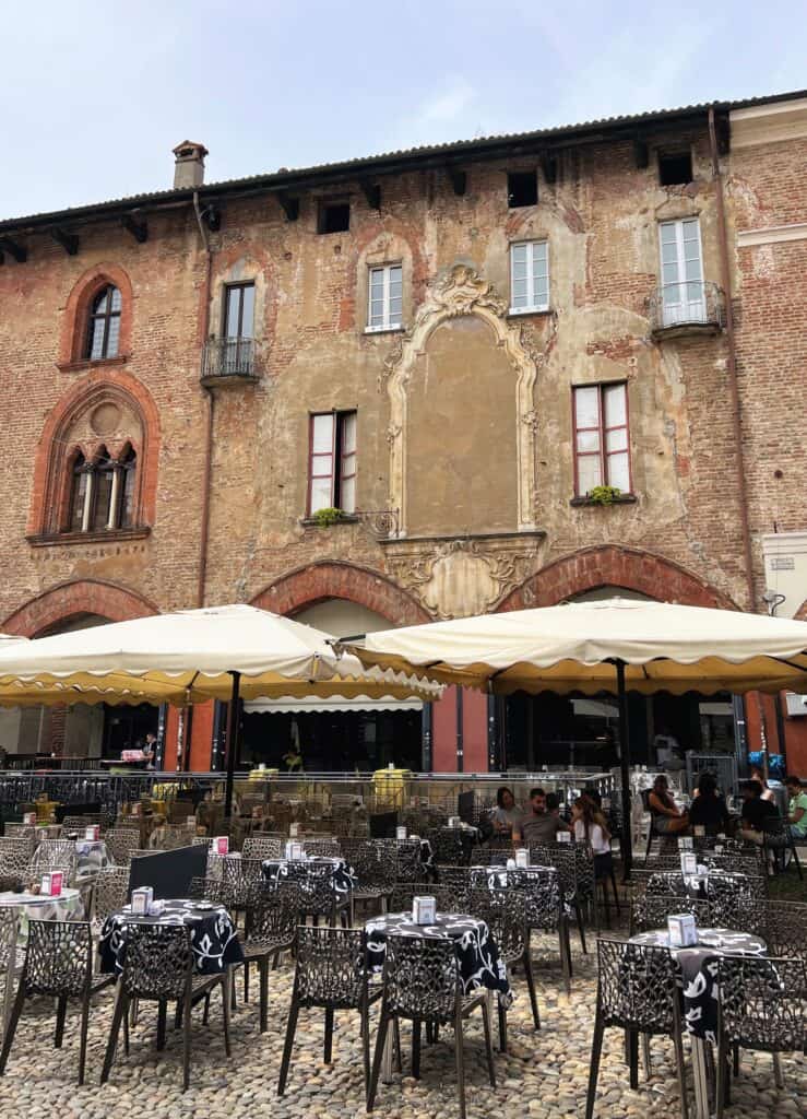 Pavia Outdoor Cafe With Tables And White Umbrellas Medieval Brick Building Facades With Ornate Carvings