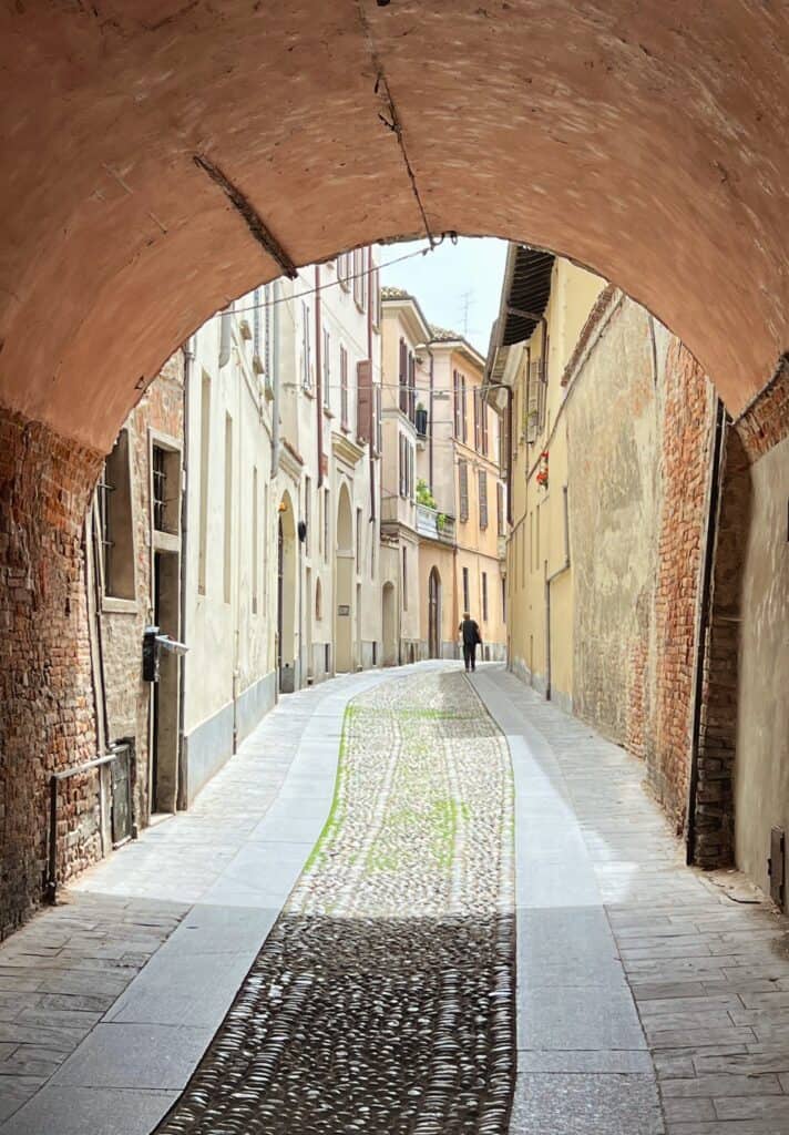 Pavia Cobblestone Street Under Arched Tunnel Pastel Houses Pedestrian In Distance