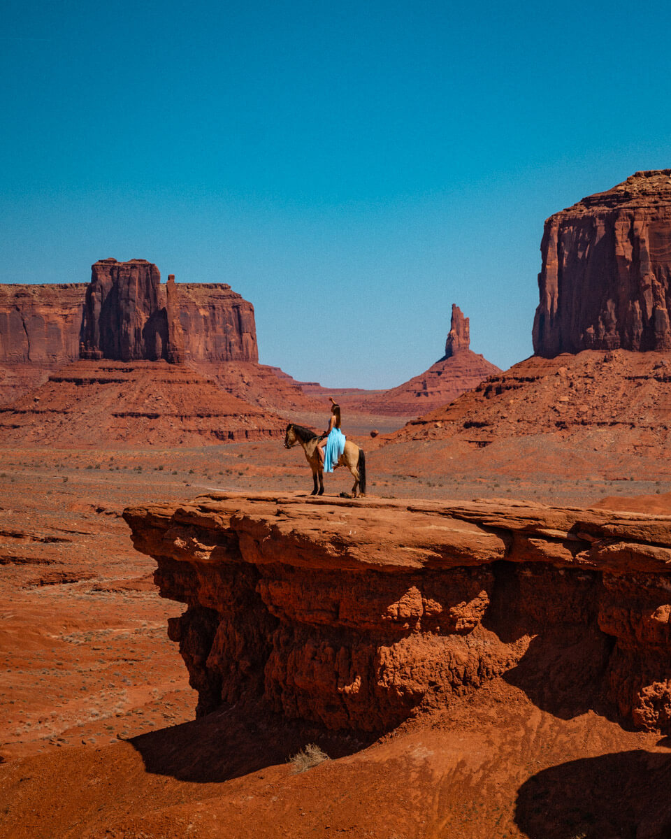 girl with blue dress sitting in a horse at the John fords view point in monument valley, USA